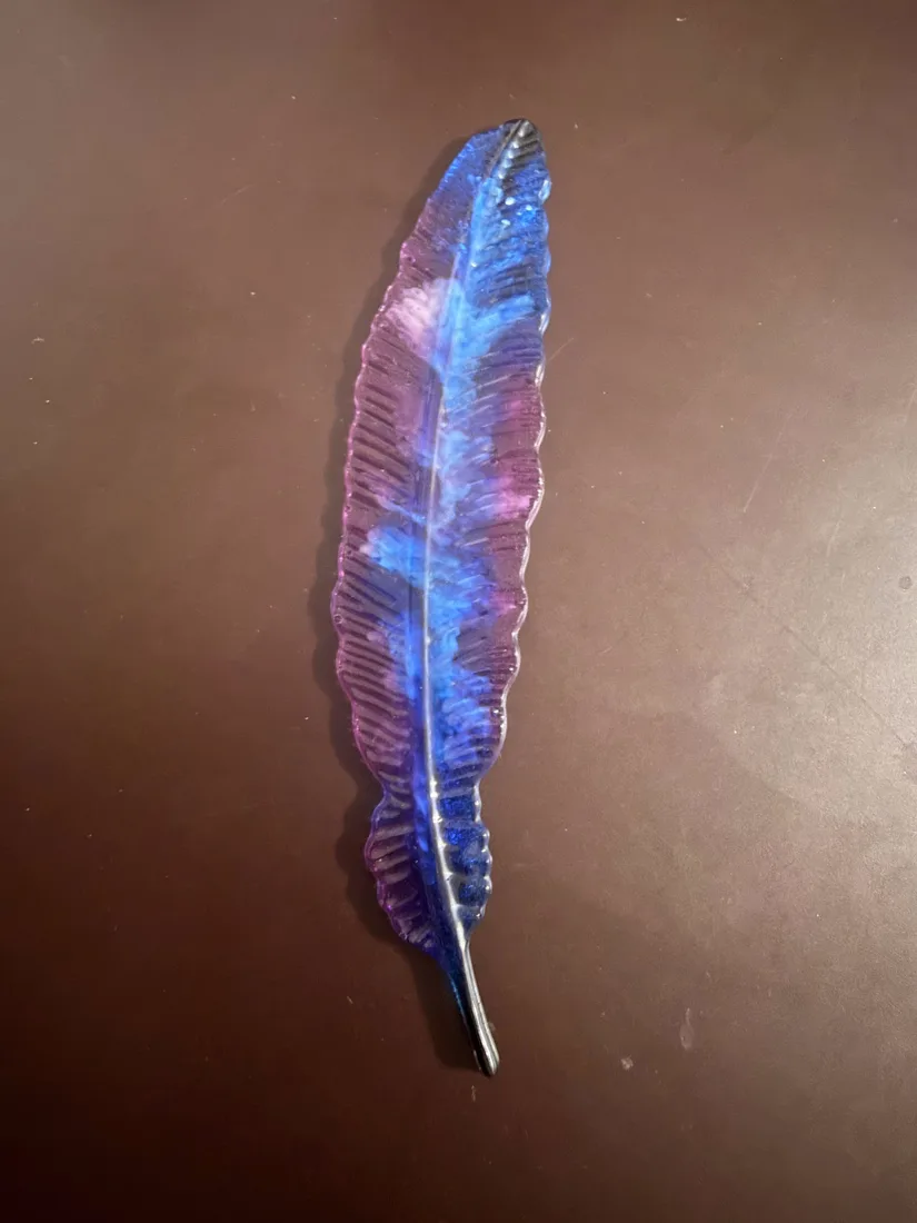 Handmade resin feather art piece laying flat, blue and violet tones