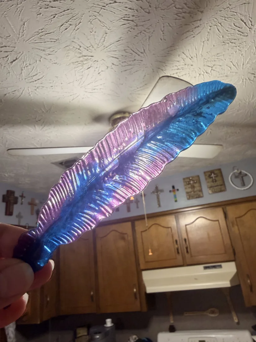 Handmade resin feather art piece held up to the light